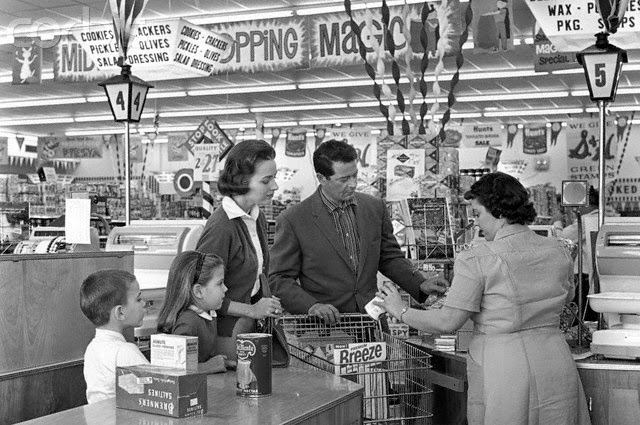 Family at a grocery store checkout line, clerk behind the counter.